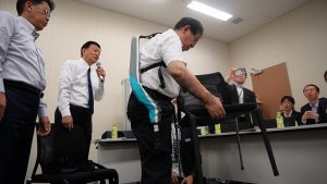 （左：株式会社ダイドーの腕用アシストスーツ「TASK AR」着用。右：イノフィスの腰用アシストスーツ「マッスルスーツ Exo-Power」着用） 